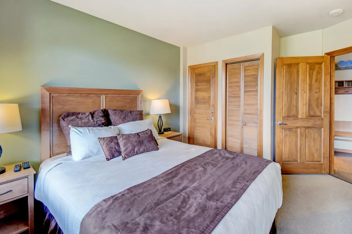 A cozy bedroom featuring a plush queen bed with decorative pillows, a nightstand, and stylish lighting. The neutral palette and soft textures evoke a sense of calm and comfort, ideal for guests or children.