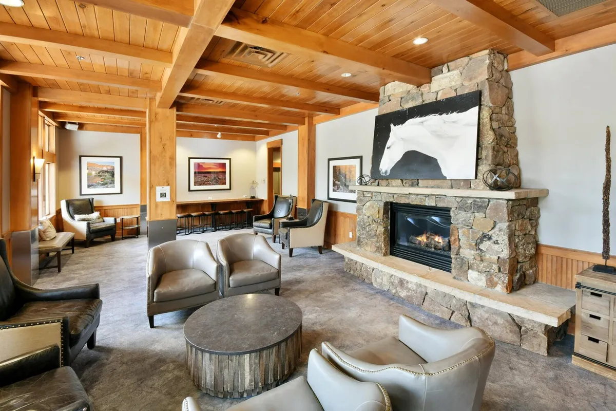 An inviting lobby living room with comfortable seating gathered around a grand stone fireplace. The setting is cozy, perfect for socializing, reading, or enjoying a warm drink after a day of mountain adventures. Local artwork and soft lighting enhance the welcoming ambiance.