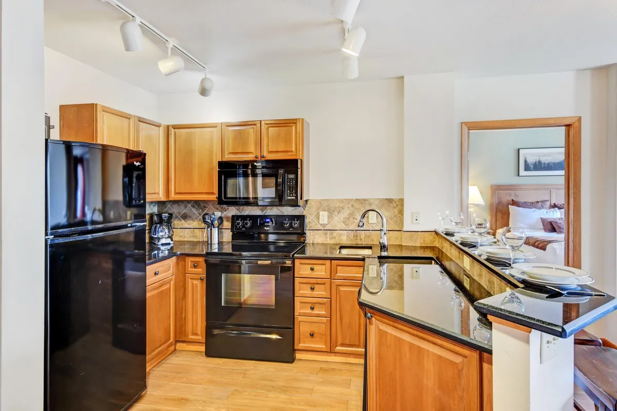 A close-up of the modern kitchen featuring black appliances, a granite countertop, and warm wooden cabinetry. The space is designed for cooking, entertaining, and creating memorable meals together.