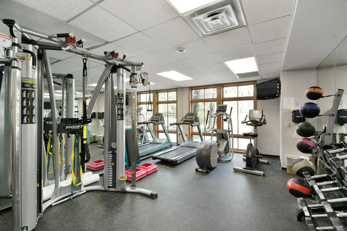 An interior fitness center filled with modern exercise machines, a mirrored wall, and large windows letting in natural light. The environment feels motivating and well-equipped, encouraging guests to maintain their routines or enjoy wellness activities during their stay.